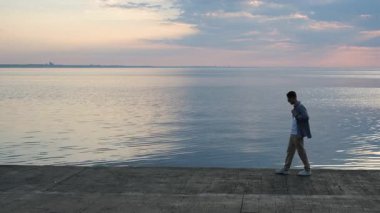 Genç bir adam şafak vakti setin kenarında yürüyor.