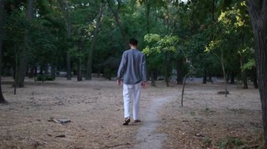 Genç yakışıklı bir adam yaz günü gün doğumunda parkta yürüyor.