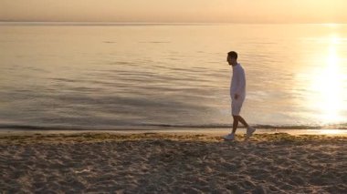 Genç yakışıklı adam gün doğumunda deniz kıyısında koşuyor.