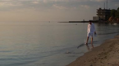 Genç yakışıklı adam gün doğumunda deniz kıyısında koşuyor.