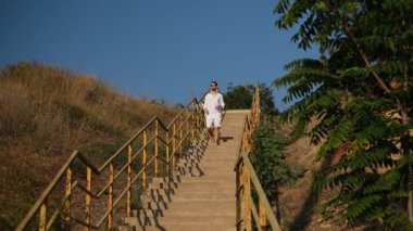 Genç bir adam güneşli bir yaz gününde yavaşça sahile doğru yürür.