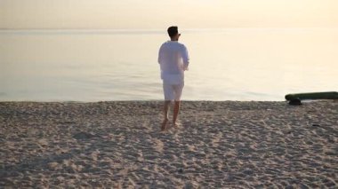 Genç yakışıklı adam bir yaz günü şafak vakti sahilin kenarında yürüyor.