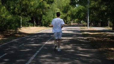 Genç bir adam güneşli bir yaz gününde parkta koşuyor.