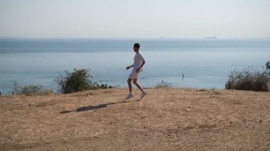 Genç sporcu bir yaz günü deniz kenarındaki yamaçlarda koşar.