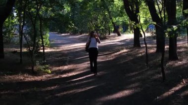 Genç bir kadın yaz günü şafak vakti parkta yürüyor.