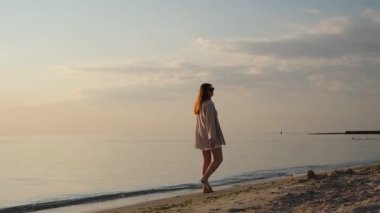 Deniz kıyısında yürüyen genç kadın güneşin doğuşunun tadını çıkarıyor.