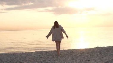 Deniz kıyısında yürüyen genç kadın güneşin doğuşunun tadını çıkarıyor.