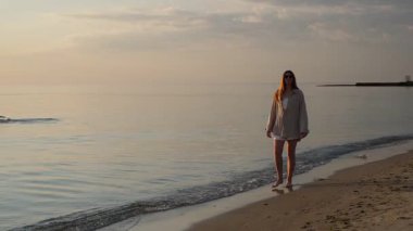 Deniz kıyısında yürüyen genç kadın güneşin doğuşunun tadını çıkarıyor.