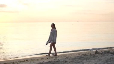 Deniz kıyısında yürüyen genç kadın güneşin doğuşunun tadını çıkarıyor.