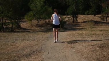 Kadın sporcu güneşli yaz gününde parkta off-road koşuyor.