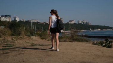 Sırt çantalı genç bir turist güneşli bir yaz gününde deniz kenarında yürüyor.