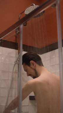 Genç esmer adam duş alıyor ve saçını yıkıyor.