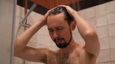 Genç esmer adam duş alıyor ve saçını yıkıyor.