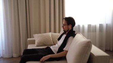 Genç esmer adam evinde kanepede dinleniyor kablosuz kulaklıkla müzik dinliyor.