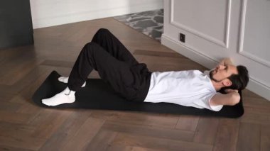 Genç esmer adam evde karın kası egzersizi yapıyor.