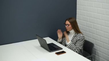 Gözlüklü genç iş kadını ofiste dizüstü bilgisayarla çalışıyor.