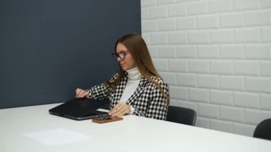 Gözlüklü genç iş kadını ofiste dizüstü bilgisayarla çalışıyor.