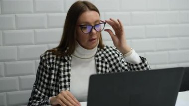 Gözlüklü genç iş kadını ofiste dizüstü bilgisayara bakarken raporda hatalar buldu.