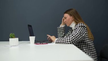 Gözlüklü genç iş kadını ofiste dizüstü bilgisayarla çalışıyor.