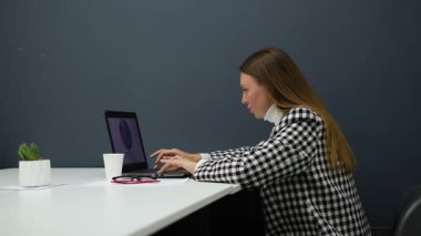 Gözlüklü genç iş kadını ofiste dizüstü bilgisayarla çalışıyor.