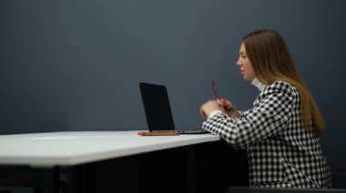 Gözlüklü genç iş kadını ofiste dizüstü bilgisayarla çalışıyor.