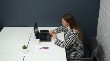 Gözlüklü genç iş kadını ofiste dizüstü bilgisayarla çalışıyor.