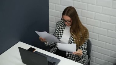 Genç bir kadın dizüstü bilgisayarında oturan belgeleri inceliyor.