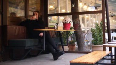 Genç bir kadın yağmurlu bir sonbahar gününde kafe terasında matcha içiyor.