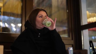 Genç bir kadın yağmurlu bir sonbahar gününde kafe terasında matcha içiyor.