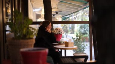 Genç bir kadın yağmurlu bir sonbahar gününde kafe terasında matcha içiyor.
