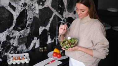 Güzel genç bir kadın sabah erkenden mutfağında taze sebze salatası hazırlıyor.