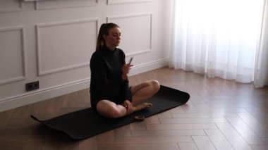 Evde yoga minderinde meditasyon yapan genç bir kadın rahatlamak için aromatik tütsü çubuğu yakıyor.