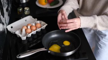 Güneşli bir mutfakta çırpılmış yumurta pişiren genç bir kadın.