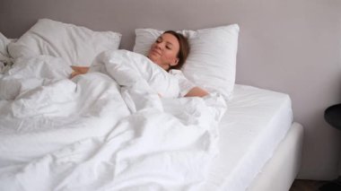 Uykulu genç kadın uyanıyor ve güneş ışığında esniyor, rahat bir sabah atmosferi var.