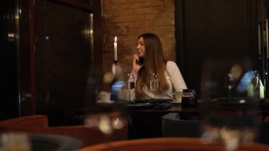 Uzun saçlı genç bir kadın restoran masasında yalnız başına yemek için kendisine eşlik edecek birini bekliyor.