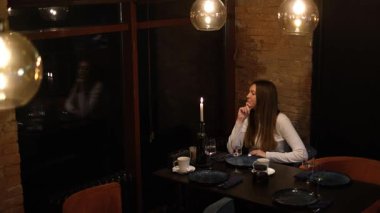 Uzun saçlı genç bir kadın restoran masasında yalnız başına yemek için kendisine eşlik edecek birini bekliyor.