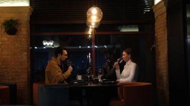 Genç bir çift restoranda yemek yiyor ve şarap içiyor.