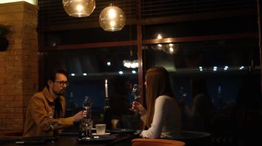 Genç bir çift restoranda yemek yiyor ve şarap içiyor.