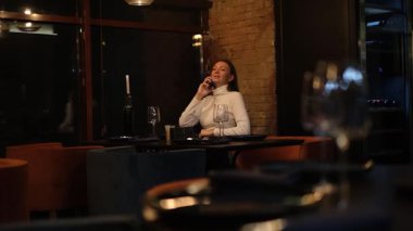 Uzun saçlı genç bir kadın restoran masasında yalnız başına yemek için kendisine eşlik edecek birini bekliyor.