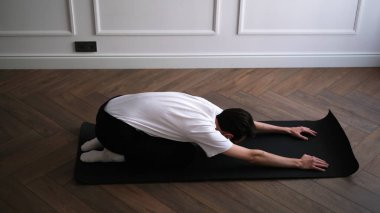 Koyu saçlı genç adam sabahın erken saatlerinde evde yoga yapıyor.