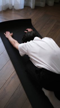 Koyu saçlı genç adam sabahın erken saatlerinde evde yoga yapıyor.