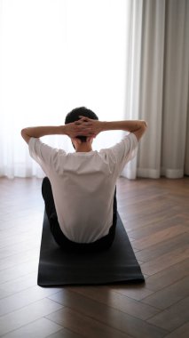 Koyu renk saçlı genç adam sabahın köründe evde egzersiz yapıyor.