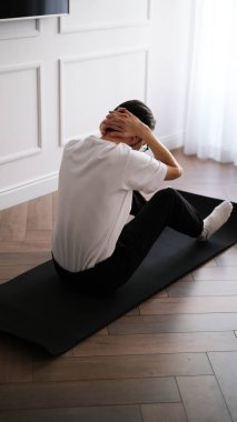 Koyu renk saçlı genç adam sabahın köründe evde egzersiz yapıyor.