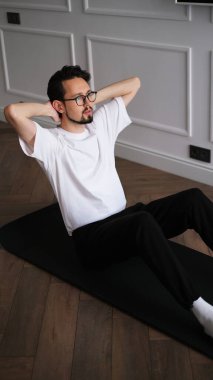 Koyu renk saçlı genç adam sabahın köründe evde egzersiz yapıyor.