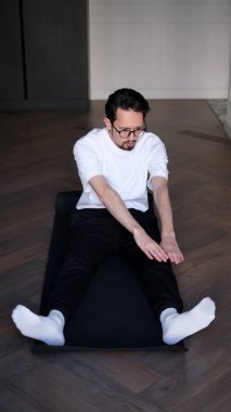 Koyu renk saçlı genç adam sabahın köründe evde egzersiz yapıyor.