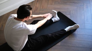 Koyu renk saçlı genç adam sabahın köründe evde egzersiz yapıyor.