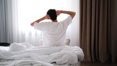 Genç esmer adam yataktan sonra geriniyor.