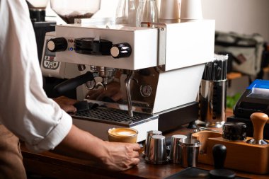 Bir kahveci, rahat bir kahve dükkanında profesyonel bir espresso makinesinde kahve hazırlar. Olay yeri, çeşitli barista araçlarıyla titiz kahve demleme sürecini yakalıyor..