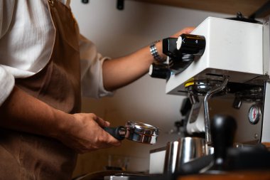 Önlüklü bir barista kahve makinesiyle kahve yapmaya hazırlanıyor..