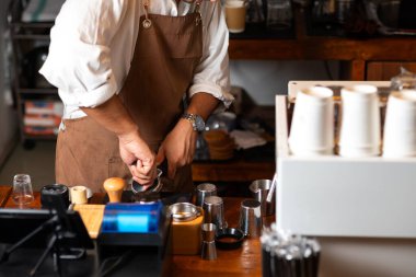 Kahve makinesinde kahve telvesi dolduran bir barista espresso demleme işlemine hazırlanıyor. Görüntü, iyi çıkarılmış bir espresso sahnesi çekmek için gereken hassasiyeti ve tekniği yakalıyor ve kahve yapma sanatını gösteriyor..